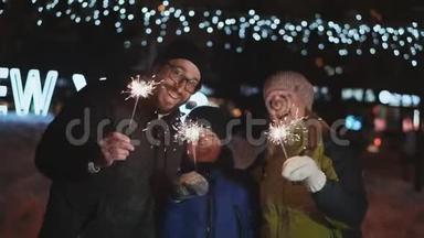 家人庆祝新年。 父亲、母亲和儿子笑着欢呼，挥舞着孟加拉火。 在街上的夜晚